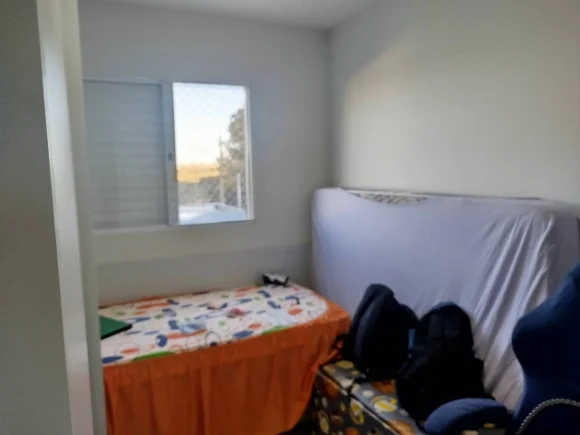 Quarto de solteiro antes: cama com colcha amassada e mochilas empilhadas no canto.